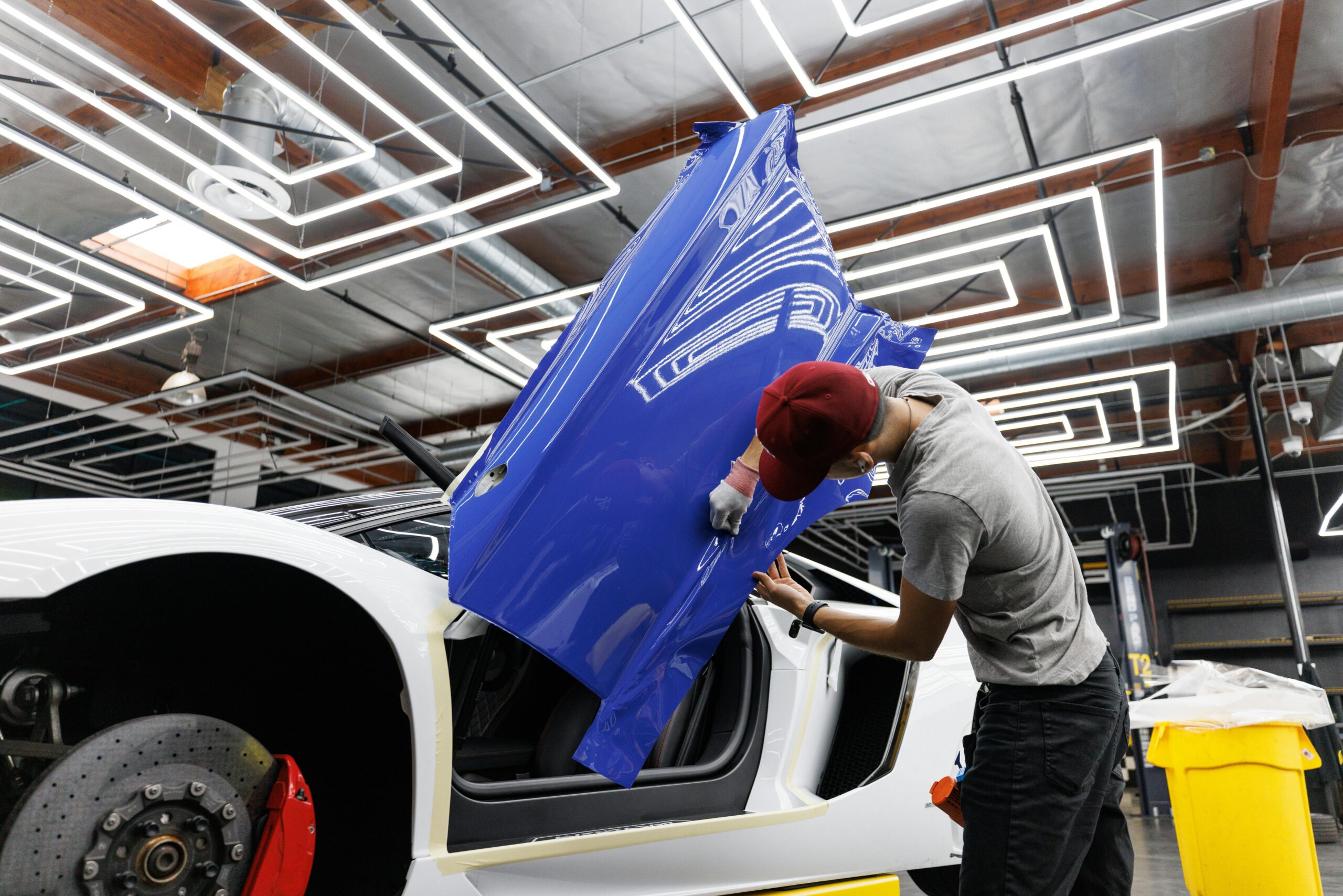 Auto mechanic applying blue vinyl wrap to a car door in a modern garage.